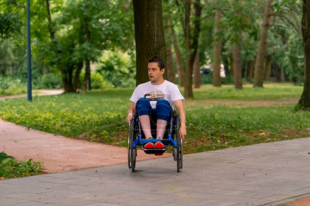 Téléchargez les photos : Inclusivité Un homme handicapé fait des cascades en fauteuil roulant dans un parc municipal sur fond d'arbres - en image libre de droit