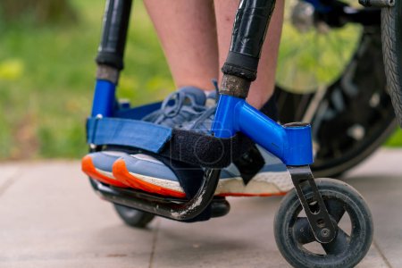Téléchargez les photos : Inclusivité Gros plan sur les jambes d'un homme handicapé qui conduit un fauteuil roulant dans un parc municipal - en image libre de droit