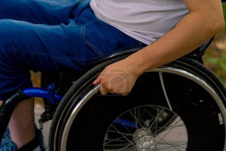 Téléchargez les photos : Inclusivité Gros plan de la main d'un homme handicapé qui roule en fauteuil roulant dans un parc municipal - en image libre de droit