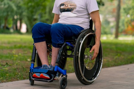 Foto de Inclusividad Un joven con discapacidad monta en una silla de ruedas en un parque de la ciudad sobre un fondo de árboles - Imagen libre de derechos