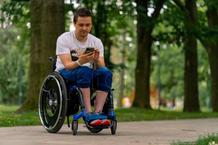 Photo for Inclusiveness Focused A man with disabilities in a wheelchair stares into a smartphone he is holding in city park with trees in the background - Royalty Free Image