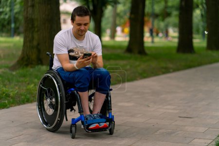 Photo for Inclusiveness Focused A man with disabilities in a wheelchair stares into a smartphone he is holding in city park with trees in the background - Royalty Free Image