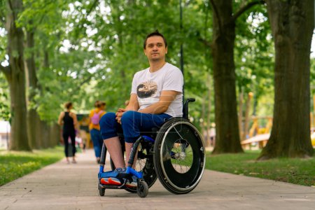 Foto de Inclusividad Retrato de un joven con discapacidad en silla de ruedas en un parque de la ciudad sobre el fondo de los árboles - Imagen libre de derechos