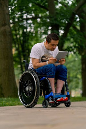Photo for Inclusiveness A man with disabilities in wheelchair stares intently at the tablet he is holding in the park - Royalty Free Image