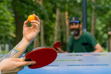 Foto de Un primer plano de una pelota de ping-pong que se sirve en el fondo de un hombre mayor con barba gris que se prepara para patear la pelota - Imagen libre de derechos