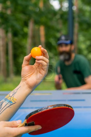 Téléchargez les photos : Gros plan d'une balle de ping-pong servie sur le fond d'un homme plus âgé à la barbe grise qui se prépare à frapper la balle - en image libre de droit