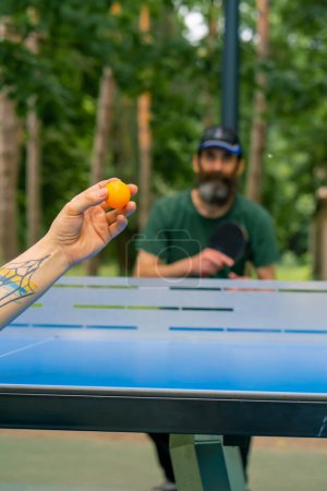 Téléchargez les photos : Gros plan d'une balle de ping-pong servie sur le fond d'un homme plus âgé à la barbe grise qui se prépare à frapper la balle - en image libre de droit