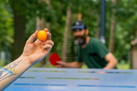 Foto de Un primer plano de una pelota de ping-pong que se sirve en el fondo de un hombre mayor con barba gris que se prepara para patear la pelota - Imagen libre de derechos