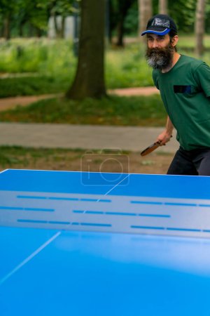 Téléchargez les photos : Inclusivité Un homme âgé aux cheveux longs et à la barbe grise joue au ping-pong dans le parc de la ville - en image libre de droit