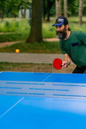 Téléchargez les photos : Inclusivité Un homme âgé aux cheveux longs et à la barbe grise joue au ping-pong dans le parc de la ville - en image libre de droit