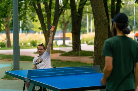 Foto de Inclusividad Feliz Un hombre discapacitado en silla de ruedas juega ping pong contra un anciano con barba gris en el parque de la ciudad - Imagen libre de derechos