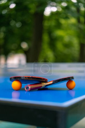 Foto de Dos raquetas de tenis y dos pelotas de tenis naranja se encuentran en una mesa de tenis azul junto a una red en el parque de la ciudad ping pong primer plano - Imagen libre de derechos