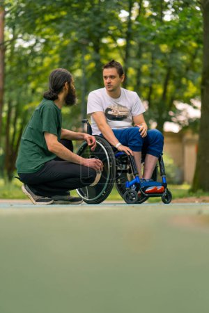 Téléchargez les photos : Inclusivité Un homme handicapé communique avec un homme âgé aux cheveux longs et à la barbe grise dans un parc urbain avec des arbres en arrière-plan - en image libre de droit
