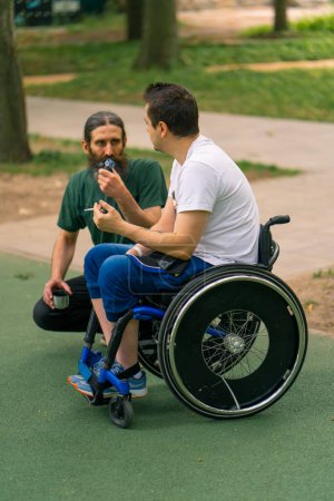 Téléchargez les photos : Inclusivité Un homme handicapé interagit avec un homme âgé qui fume une pipe dans un parc municipal sur fond d'arbres - en image libre de droit