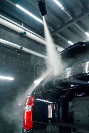 Close-up of a male car wash employee washing the rear window of a black luxury car with high-pressure washer