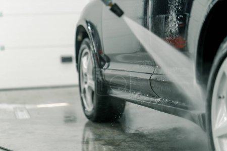 Téléchargez les photos : Gros plan d'un employé de lavage de voiture qui lave les rebords d'une voiture de luxe noire avec laveuse haute pression - en image libre de droit