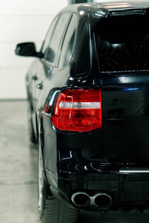 Téléchargez les photos : Close-up lavage de voiture des feux arrière et pare-chocs d'une voiture de luxe noire après le nettoyage et le nettoyage à sec dans un parking ou au centre de service de voiture - en image libre de droit