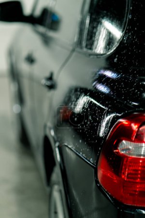 Foto de Primer plano de lavado de coches de las luces traseras y parachoques de un coche de lujo negro después de la limpieza y la limpieza en seco en un estacionamiento o en el centro de servicio de automóviles - Imagen libre de derechos