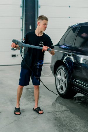 Foto de Un empleado de lavado de autos masculino lava un auto de lujo negro con lavadora de alta presión en la bahía de lavado de autos - Imagen libre de derechos
