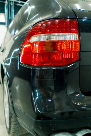 Téléchargez les photos : Close-up lavage de voiture des feux arrière et pare-chocs d'une voiture de luxe noire après le nettoyage et le nettoyage à sec dans un parking ou au centre de service de voiture - en image libre de droit
