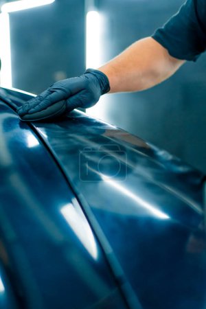 Téléchargez les photos : Gros plan d'un ouvrier de lavage de voiture en gants noirs polissant le capot et le phare d'une luxueuse voiture noire avec une éponge de polissage de voiture - en image libre de droit