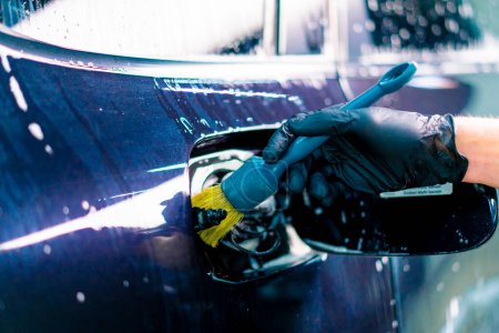 Foto de Primer plano de un empleado de lavado de autos lavando el espacio de la tapa de combustible de un automóvil azul de lujo usando un cepillo - Imagen libre de derechos
