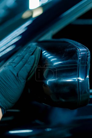 Photo for Focused Male car wash worker in black gloves polishes the mirror of a luxury blue car using polishing sponge car care concept  Close-up - Royalty Free Image