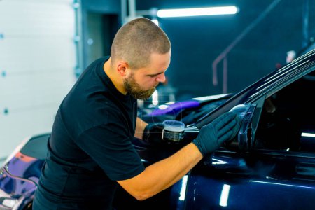 Photo for Focused Male car wash worker in black gloves polishes the mirror of a luxury blue car using polishing sponge car care concept - Royalty Free Image