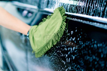 Foto de Primer plano de un trabajador de lavado de coches utilizando un paño verde para lavar el coche de lujo negro con champú de lavado de coches - Imagen libre de derechos