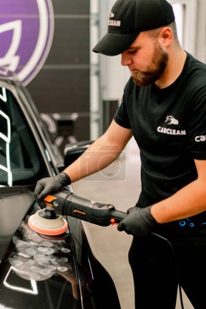 Foto de Primer plano de un trabajador de lavado de coches utilizando una máquina de pulido para pulir la capucha de un coche de lujo negro - Imagen libre de derechos