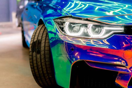Foto de Primer plano de la rueda del faro y parachoques del coche de lujo cubierto con película protectora en color camaleón en el lavado de coches - Imagen libre de derechos