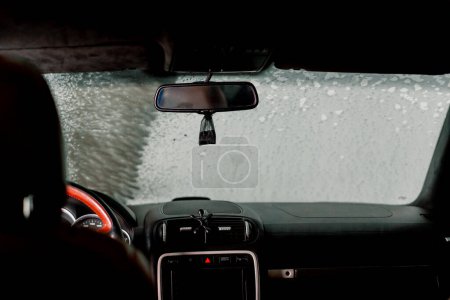 Téléchargez les photos : Un gros plan du pare-brise et de l'intérieur d'une voiture de luxe au moment du lavage de la voiture à l'aide de mousse et d'un nettoyeur sous pression - en image libre de droit