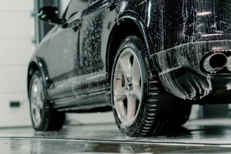 Primer plano de la aplicación de espuma de coche en el neumático trasero del coche de lujo negro en la caja de lavado del coche del concepto de cuidado del coche