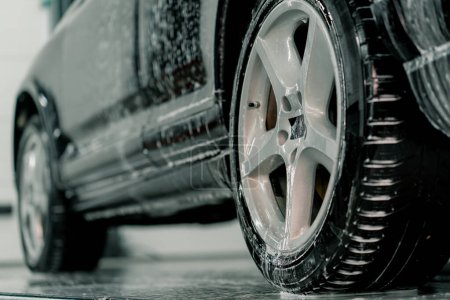 Foto de Primer plano de la aplicación de espuma de coche en el neumático trasero del coche de lujo negro en la caja de lavado del coche del concepto de cuidado del coche - Imagen libre de derechos