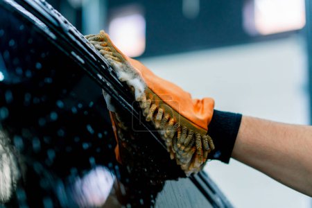 Foto de Primer plano de un trabajador de lavado de coches utilizando un paño de microfibra para lavar el coche de lujo negro con champú de lavado de coches - Imagen libre de derechos