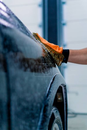 Téléchargez les photos : Gros plan d'un ouvrier de lavage de voiture utilisant un chiffon en microfibre pour laver une voiture de luxe noire avec un shampooing de lavage de voiture - en image libre de droit