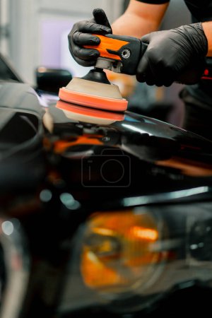 Foto de Primer plano de un trabajador de lavado de coches utilizando una máquina de pulido para pulir la capucha de un coche de lujo negro - Imagen libre de derechos