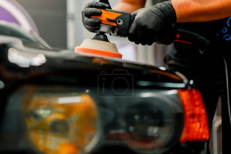 Téléchargez les photos : Gros plan d'un employé de lavage de voiture utilisant une polisseuse pour polir le capot d'une voiture de luxe noire - en image libre de droit