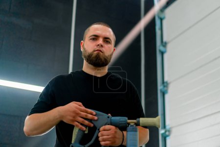 Téléchargez les photos : Portrait d'un homme sérieux avec la barbe d'un ouvrier de lavage de voiture qui tient la buse du générateur de mousse dans ses mains concept de soins de voiture - en image libre de droit