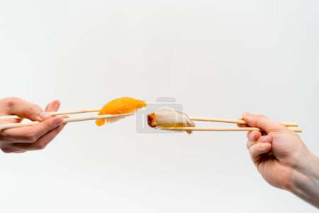 Photo for Close-up of men's hands with chopsticks holding eel sushi and salmon sushi in the air in front of each other on white background - Royalty Free Image