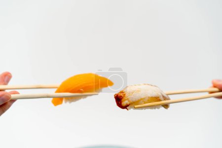 Foto de Primer plano de las manos de los hombres con palillos que sostienen sushi de anguila y sushi de salmón en el aire frente al otro sobre fondo blanco - Imagen libre de derechos