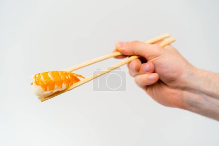 Photo for Close-up of a man's hand with chopsticks holding shrimp sushi in the air on white background - Royalty Free Image