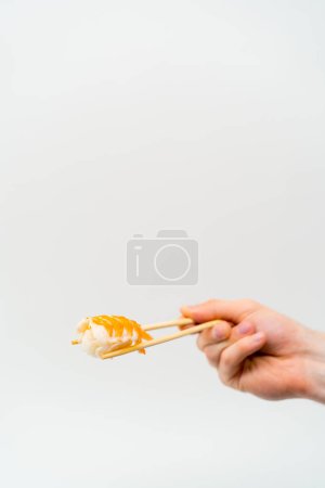 Foto de Primer plano de la mano de un hombre con palillos que sostienen el sushi de camarones en el aire sobre fondo blanco - Imagen libre de derechos