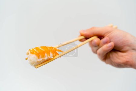 Foto de Primer plano de la mano de un hombre con palillos que sostienen el sushi de camarones en el aire sobre fondo blanco - Imagen libre de derechos