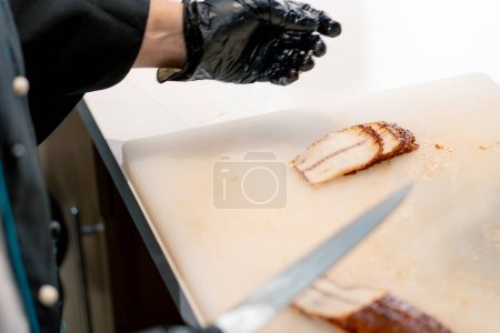 Téléchargez les photos : Gros plan d'un chef sushi en gants coupant un filet d'anguille avec un couteau professionnel sur la table de cuisine tout en faisant des sushis - en image libre de droit