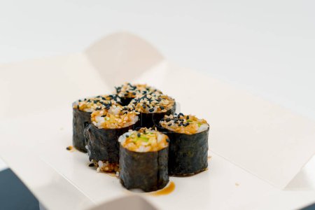 Foto de Primer plano del rollo maki con aguacate con salsa de soja en caja de entrega de sushi sobre fondo blanco - Imagen libre de derechos