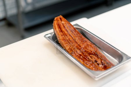 Foto de Primer plano de un filete de anguila marinada acostado en una bandeja profesional sobre una mesa de cocina en la cocina del restaurante de sushi - Imagen libre de derechos