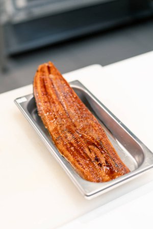 Téléchargez les photos : Gros plan d'un filet d'anguille mariné couché sur un plateau professionnel sur une table de cuisine dans la cuisine du restaurant de sushi - en image libre de droit