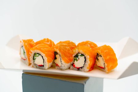 Foto de Primer plano de un rollo de filigrana con pepino de salmón y requesón sobre un fondo blanco en una caja de sushi - Imagen libre de derechos