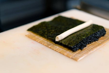 Foto de Primer plano de un chef de sushi esparciendo queso crema sobre arroz negro en una hoja de nori en el proceso de hacer rollos en la cocina del restaurante de sushi - Imagen libre de derechos